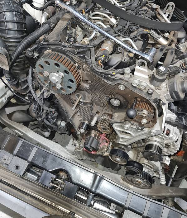 Engine with front timing cover removed showing exposed timing chain, camshaft sprockets and crankshaft components